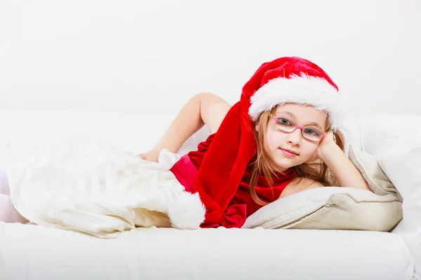 Christmas girl in santa hat lying on sofa — Stock Photo, Image