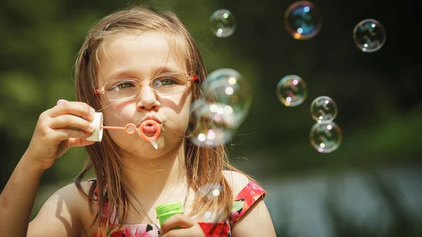 Kleines Mädchen hat Spaß beim Blasen von Seifenblasen im Park. — Stockfoto