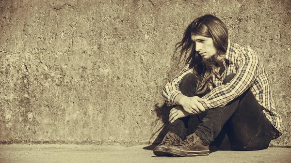 Adam uzun saçlı oturma rahat grunge duvara üzgün — Stok fotoğraf
