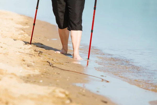 Старшая женщина, практикующая северную ходьбу по берегу моря — стоковое фото
