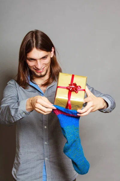 Kerl steckt verpacktes Geschenk in gestrickte Weihnachtssocke — Stockfoto