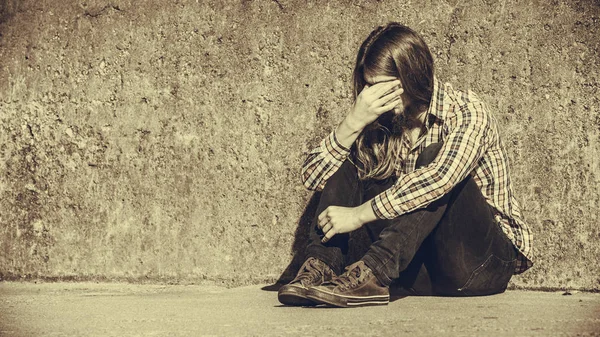 Mann mit langen Haaren sitzt traurig allein auf Grunge-Wand — Stockfoto