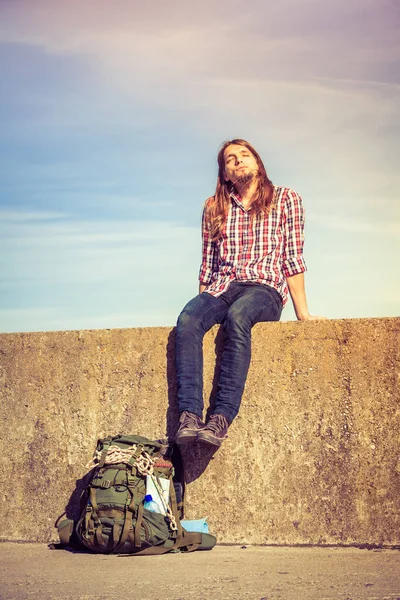 Hombre mochilero turístico sentado en la pared grunge al aire libre —  Fotos de Stock