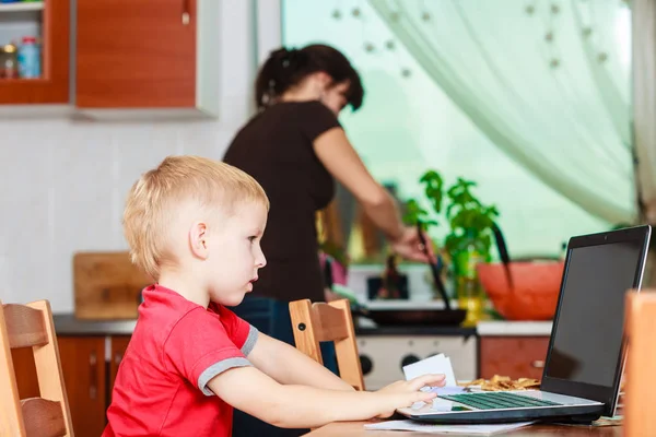 Jongetje met laptop en moeder koken in de keuken. — Stockfoto