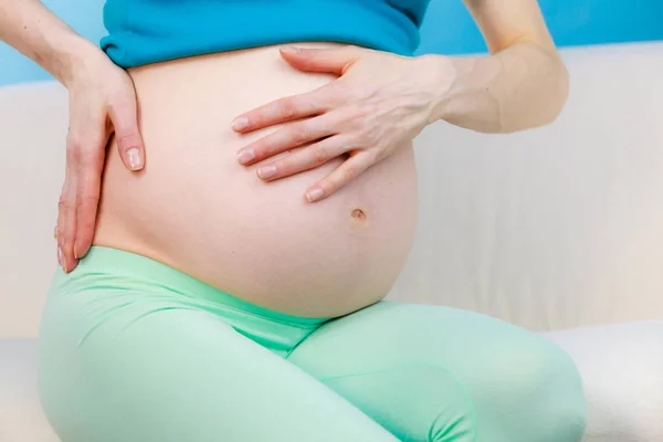 怀孕的女人坐在沙发上握着的手在她的背上 — 图库照片
