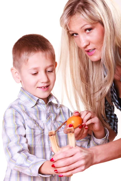 Boy with mother hold sling shot and mandarine. Royalty Free Stock Images