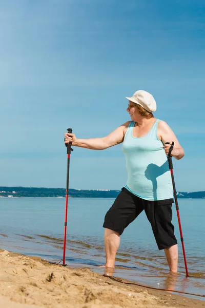 Senior woman practicing nordic walking on beach — Stock Photo, Image