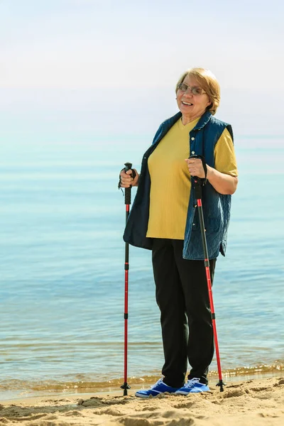 Senior woman practicing nordic walking on beach — Stock Photo, Image