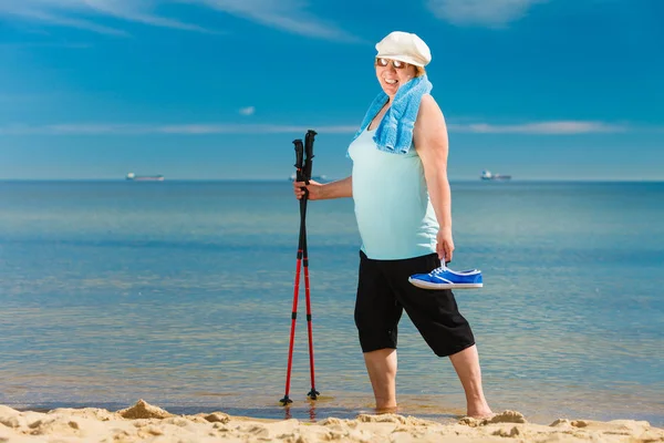 Senior woman practicing nordic walking on beach — Stock Photo, Image