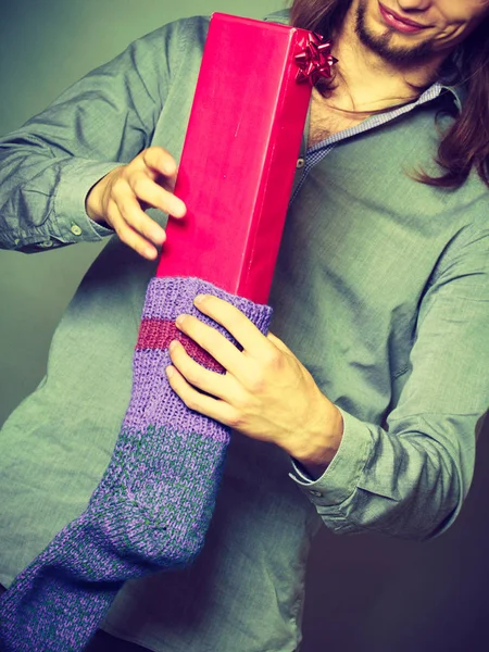 Guy putting wrapped gift in knitted christmas sock — Stock Photo, Image