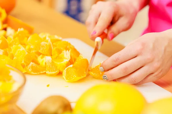 Kvinnan hemmafru i köket skär orange frukter — Stockfoto