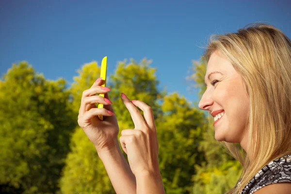 Mujer sentada en el parque, usando el teléfono tomando fotos —  Fotos de Stock