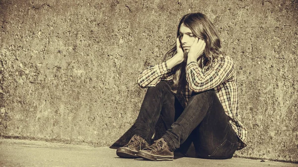 Mann mit langen Haaren sitzt traurig allein auf Grunge-Wand — Stockfoto