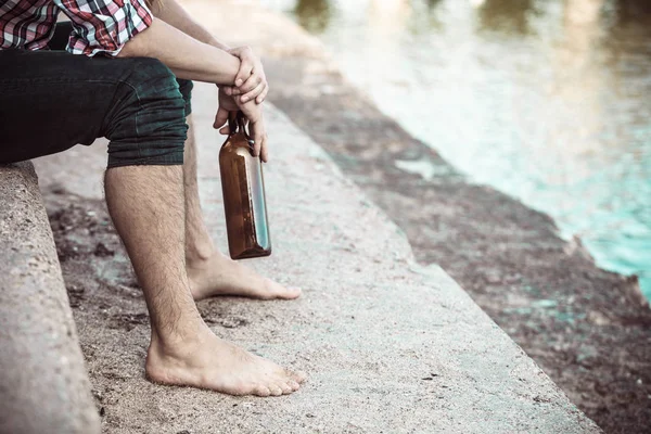 Man depressed with wine bottle sitting on beach outdoor — Stock Photo, Image