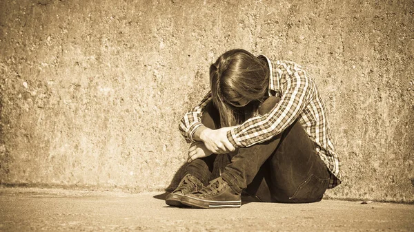 Hombre de pelo largo sentado solo triste en la pared grunge — Foto de Stock