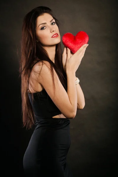 Hermosa mujer sostiene el corazón rojo en negro — Foto de Stock