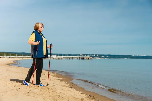 Senior woman practicing nordic walking on beach — Stock Photo, Image