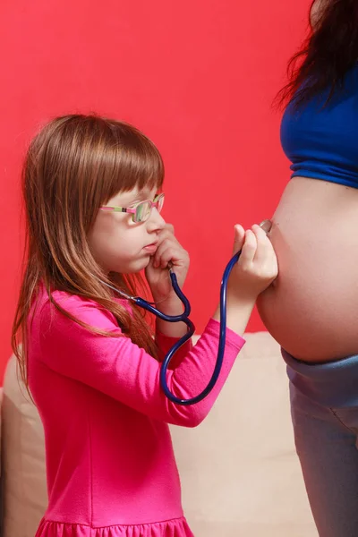 Fille utilisant le stéthoscope sur la mère enceinte — Photo