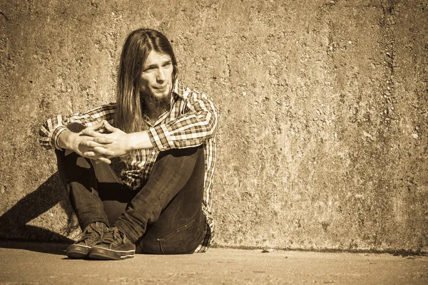 Hombre de pelo largo sentado solo triste en la pared grunge — Foto de Stock