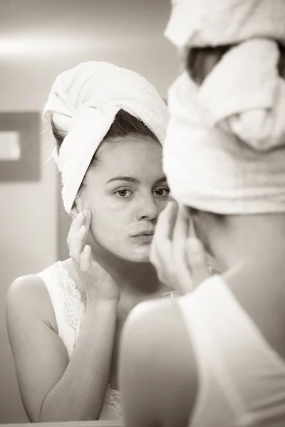 Mujer aplicando crema mascarilla en la cara en el baño —  Fotos de Stock