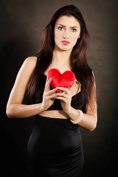 Hermosa mujer sostiene el corazón rojo en negro — Foto de Stock