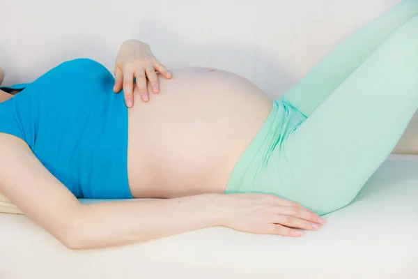 Schwangere liegt auf Couch und berührt ihren Bauch — Stockfoto