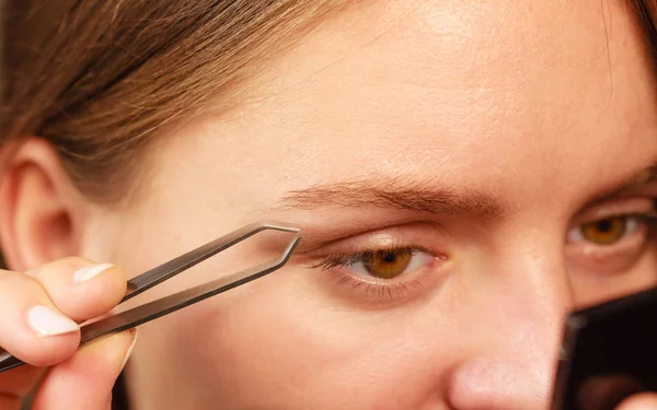 Woman tweezing eyebrows depilating with tweezers — Stock Photo, Image