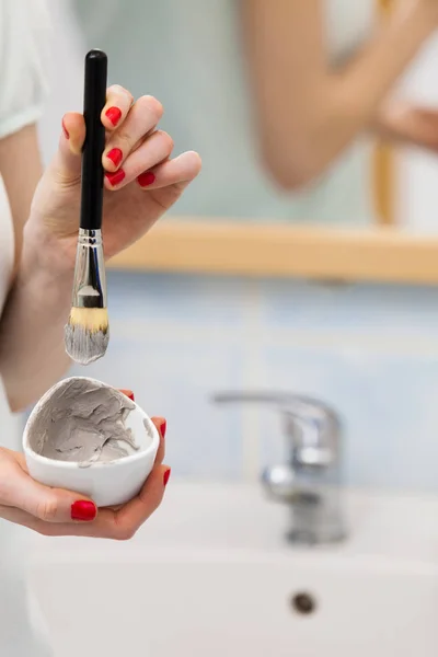 Mano femenina sosteniendo máscara de barro y cepillo. Cuidado de la piel . — Foto de Stock