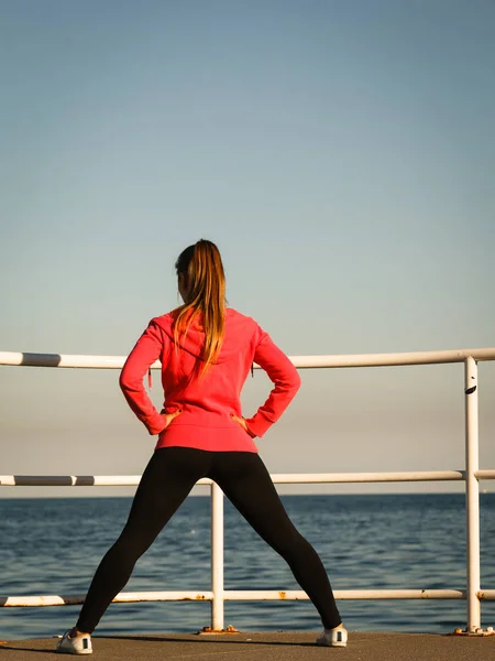 Woman jogger stretches on pier by seaside — Stock Photo, Image