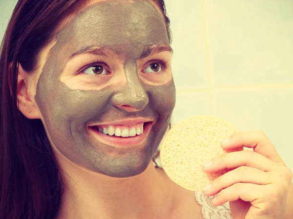 Woman with clay mask in bathroom holds sponge to remove mud — Stock Photo, Image