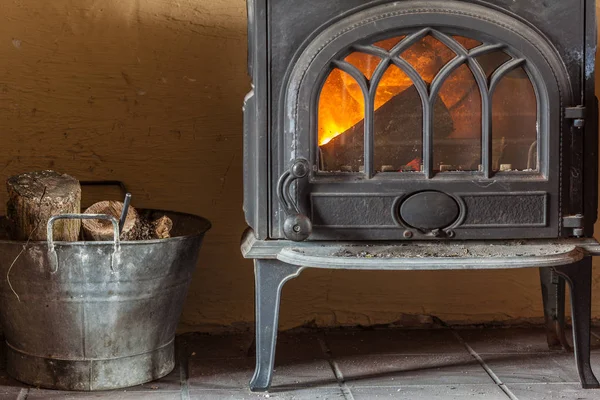 Fireplace with orange fire flame and firewood beside — Stock Photo, Image