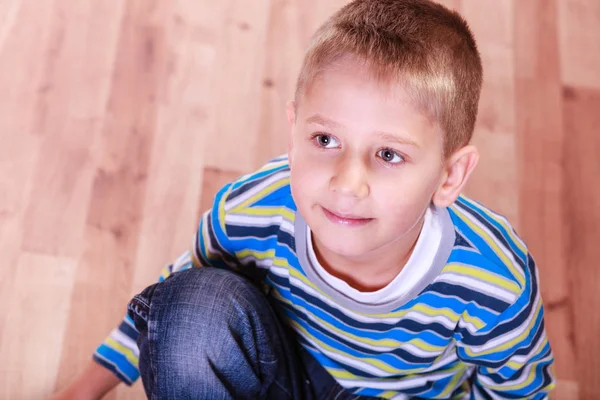 Mladý chlapec sedí na dřevěné podlahy a úsměv. — Stock fotografie