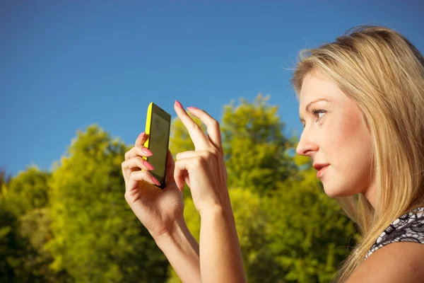 Vrouw zit in het park, met behulp van de telefoon nemen van foto 's — Stockfoto