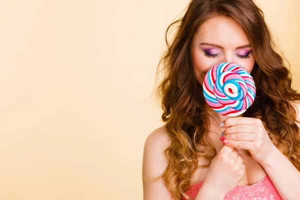 Mujer sostiene colorido caramelo piruleta en la mano, cubriendo la cara — Foto de Stock