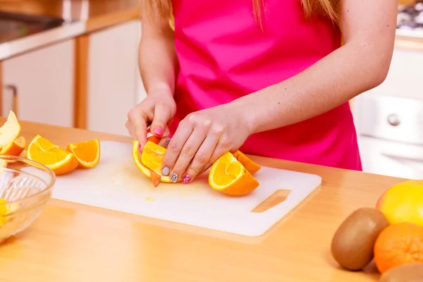 Mulher dona de casa na cozinha cortando frutas laranja — Fotografia de Stock