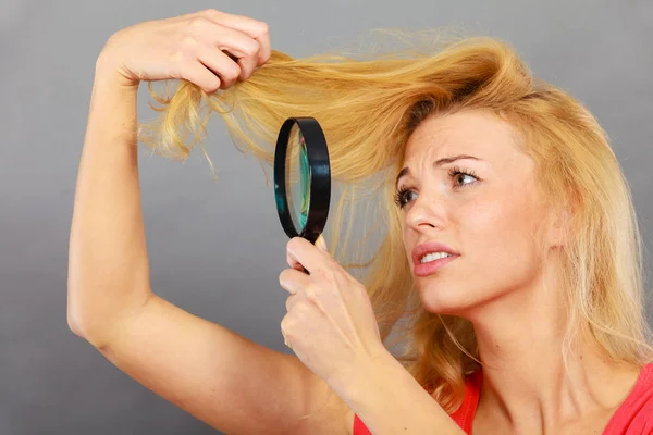 Olycklig kvinna tittar genom förstoringsglas förstört hår — Stockfoto