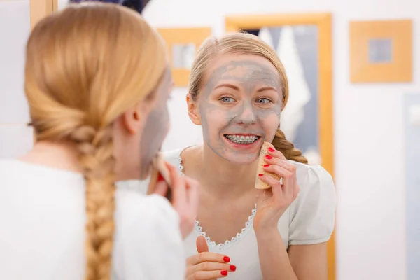 Mujer quitando la máscara facial de barro con esponja — Foto de Stock