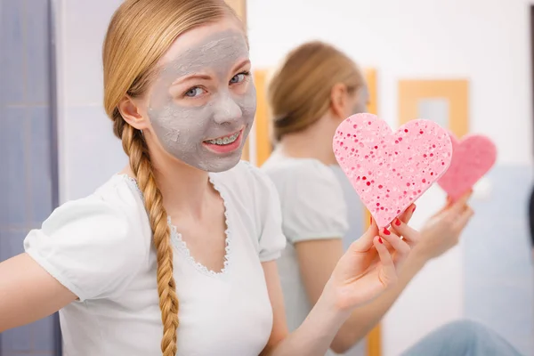 Woman having grey face mask holding heart sponge — Stock Photo, Image