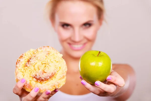 Woman holds cake and fruit in hand choosing — Stock Photo, Image