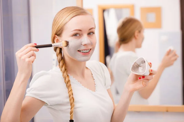 Mujer joven feliz aplicando máscara de barro en la cara —  Fotos de Stock
