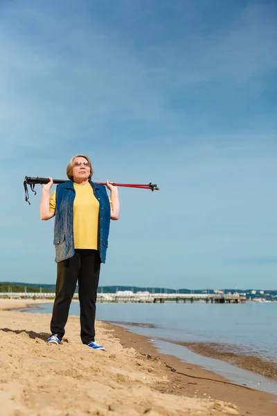 Senior woman practicing nordic walking on beach — Stock Photo, Image