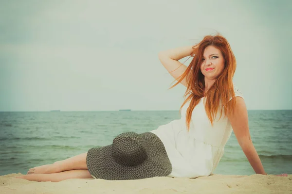 Donna rossa che tiene il cappello da sole sdraiato sulla spiaggia — Foto Stock