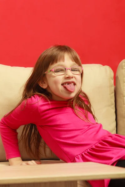 Toddler girl sitting on sofa sticking tongue out — Stock Photo, Image