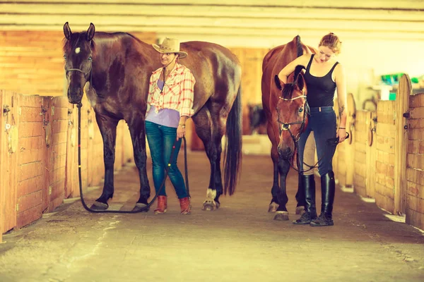 Cowgirl und Jockey gehen mit Pferden im Stall — Stockfoto