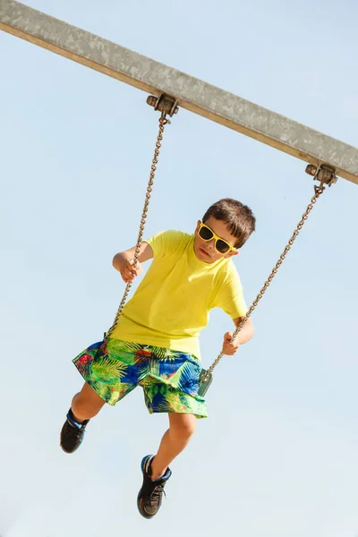 Boy playing swinging by swing-set. — Stock Photo, Image