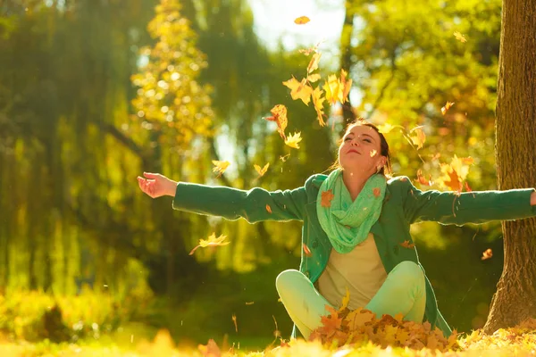 Gelukkige vrouw gooien herfst bladeren in park — Stockfoto