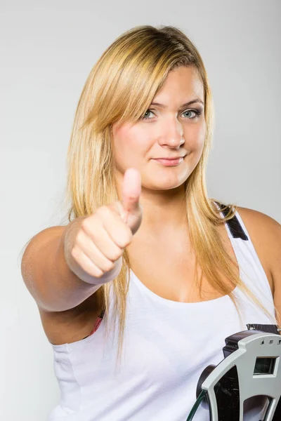Mujer feliz sosteniendo la máquina de peso mostrando el pulgar hacia arriba — Foto de Stock