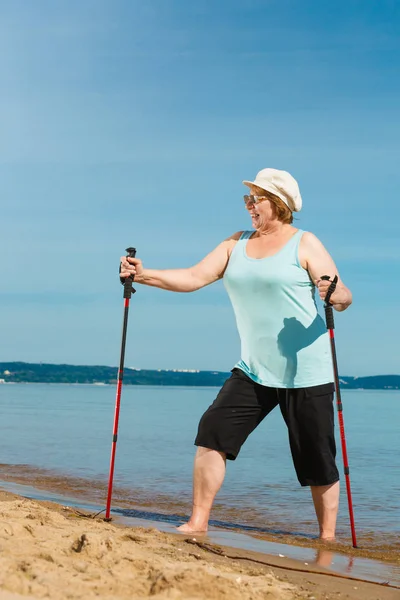 Senior Kvinna tränar stavgång på stranden — Stockfoto