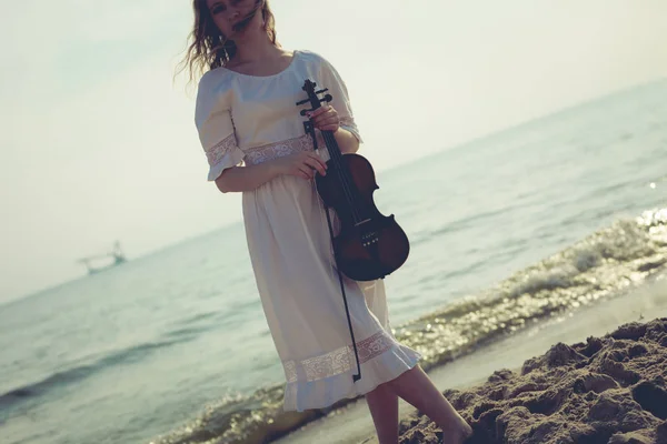 Donna sulla spiaggia vicino al mare che tiene violino — Foto Stock
