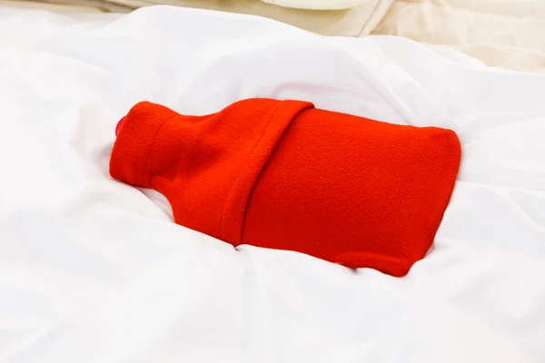 Varma röda varmvattenflaska på vita sängkläder — Stockfoto